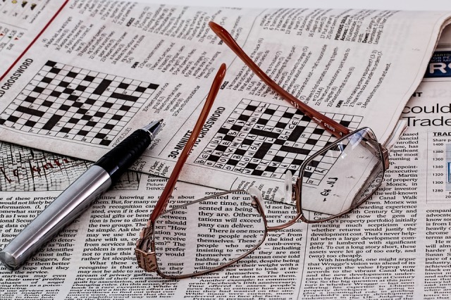 Picture of newspaper with crossword puzzle and glasses and pen lying on top